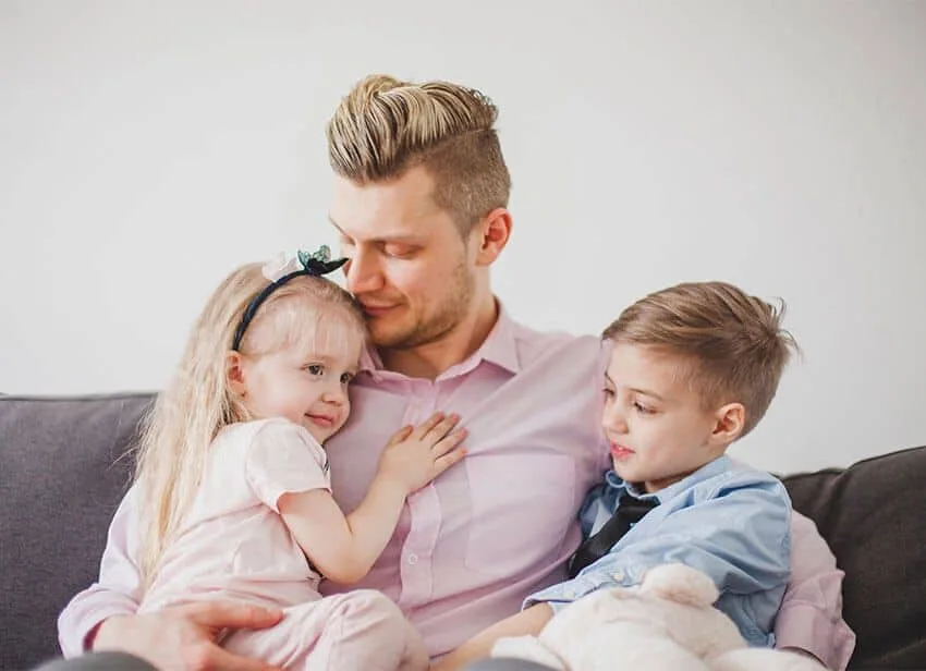 A father holding his young daughter and son on a sofa